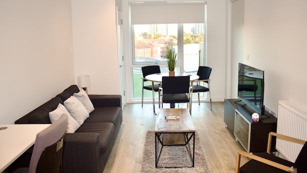 A modern living room with a sofa, a coffee table, a TV, and a dining area with chairs and a table. - Impeccable 1bed Apartment in the Heart Ofgreenford (Greenford)