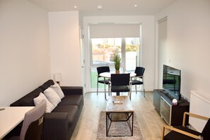 A modern living room with a sofa, a coffee table, a TV, and a dining area with chairs and a table. - Impeccable 1bed Apartment in the Heart Ofgreenford (Greenford)
