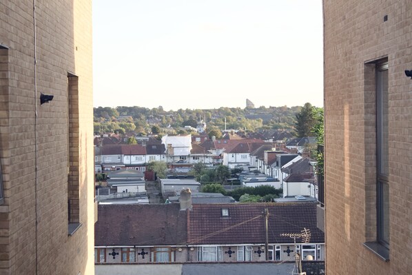 A view from a building with brick walls and large windows, overlooking a residential area with houses and a hill in the distance. - Impeccable 1bed Apartment in the Heart Ofgreenford (Greenford)