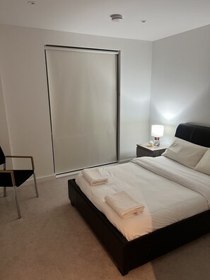 A modern bedroom with a large bed, a chair, a nightstand with a lamp, and a sliding door. - Impeccable 1bed Apartment in the Heart Ofgreenford (Greenford)
