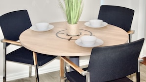 A round wooden table with four black chairs, each with a white cup and saucer. A woven basket with green plants is placed in the center. - Impeccable 1bed Apartment in the Heart Ofgreenford (Greenford)