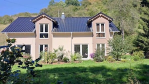A two-story house with a tiled roof, a front door, and a small garden with various plants.