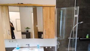 A modern bathroom with a wooden vanity, a white sink, a glass shower enclosure, and a washing machine.