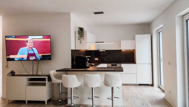 A modern kitchen with a TV, bar stools, and a dining area.