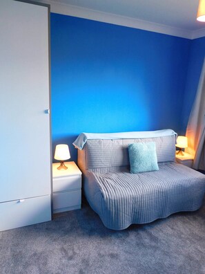 A bedroom with a bed, two bedside tables with lamps, a blue wall, and a grey carpet.