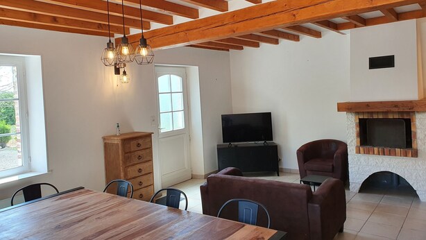 A spacious living area with a wooden ceiling, a fireplace, a television, and a dining table with chairs. - Gîte La Longère Proche de Saint-valéry, au Coeur de la Baie de Somme (Saigneville)