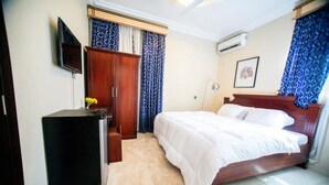 A bedroom with a bed, a wardrobe, a desk, and an air conditioning unit.