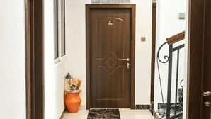A hallway with a wooden door, a potted plant, and a marble floor.