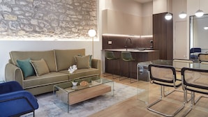 A modern living room with a stone wall, a sofa, a glass coffee table, and a dining area with chairs and a kitchen in the background. - Idiakez by FeelFree Rentals (San Sebastián)