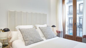 A neatly made bed with white linens and two grey pillows with a dragonfly pattern, a bedside lamp, and a view of a building through a window. - Idiakez by FeelFree Rentals (San Sebastián)