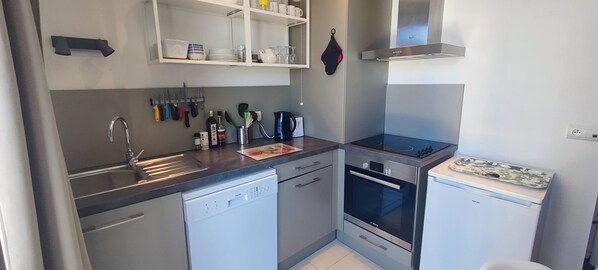 A compact kitchen with a dishwasher, oven, and sink. There are utensils hanging on the wall and a kettle on the counter.