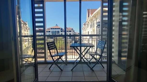 Un balcone con tavolo e sedie, da cui si gode una vista su edifici e un cielo sereno.