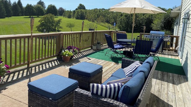 Une terrasse dotée de mobilier d’extérieur, d’un barbecue et offrant une vue sur un champ verdoyant.