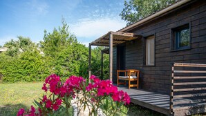 Eine Holzhütte mit Veranda, einer Bank und einem Fenster mit Blick auf einen Garten voller pinkfarbener Blumen.