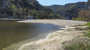 Ein Fluss mit steiniger Uferlinie und bewaldetem Hang im Hintergrund.