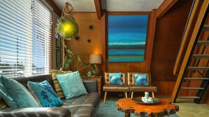 A living room with a leather sofa, two armchairs, a wooden coffee table, and a painting of a blue ocean scene. - Mermaid's Rest  Oceanfront A Frame  Pet Friendly (Otter Rock)