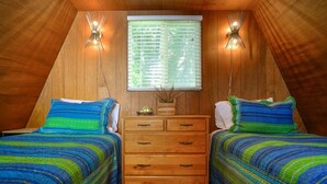 A cozy attic bedroom with two beds, wooden walls, a window with blinds, and two wall-mounted lamps. - Mermaid's Rest  Oceanfront A Frame  Pet Friendly (Otter Rock)