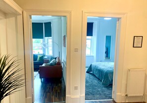 A hallway leading to two bedrooms with a blue accent wall, a radiator, and a framed certificate on the wall. - ByEvo 19 Walker GLA Apartment (Paisley)