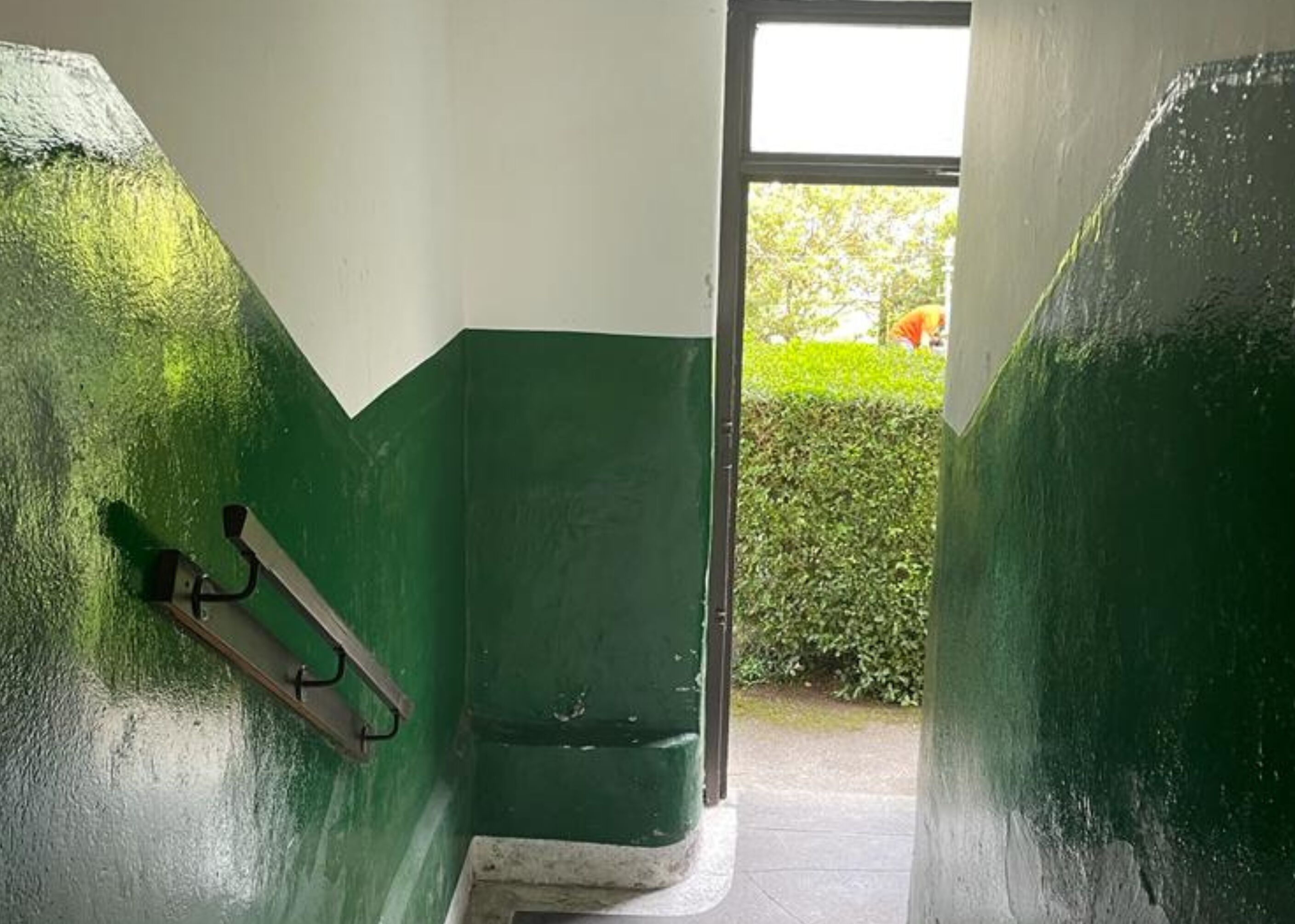 A hallway with green walls and a door leading outside.