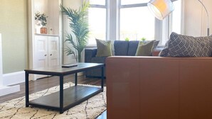 Una sala de estar con un sofá de cuero marrón, una mesa de centro de madera oscura, un armario blanco, un ventanal con vistas y una lámpara de pie.