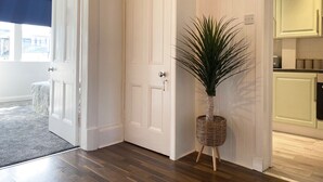 Un pasillo con una puerta cerrada, una planta en maceta y una vista parcial de una cocina.