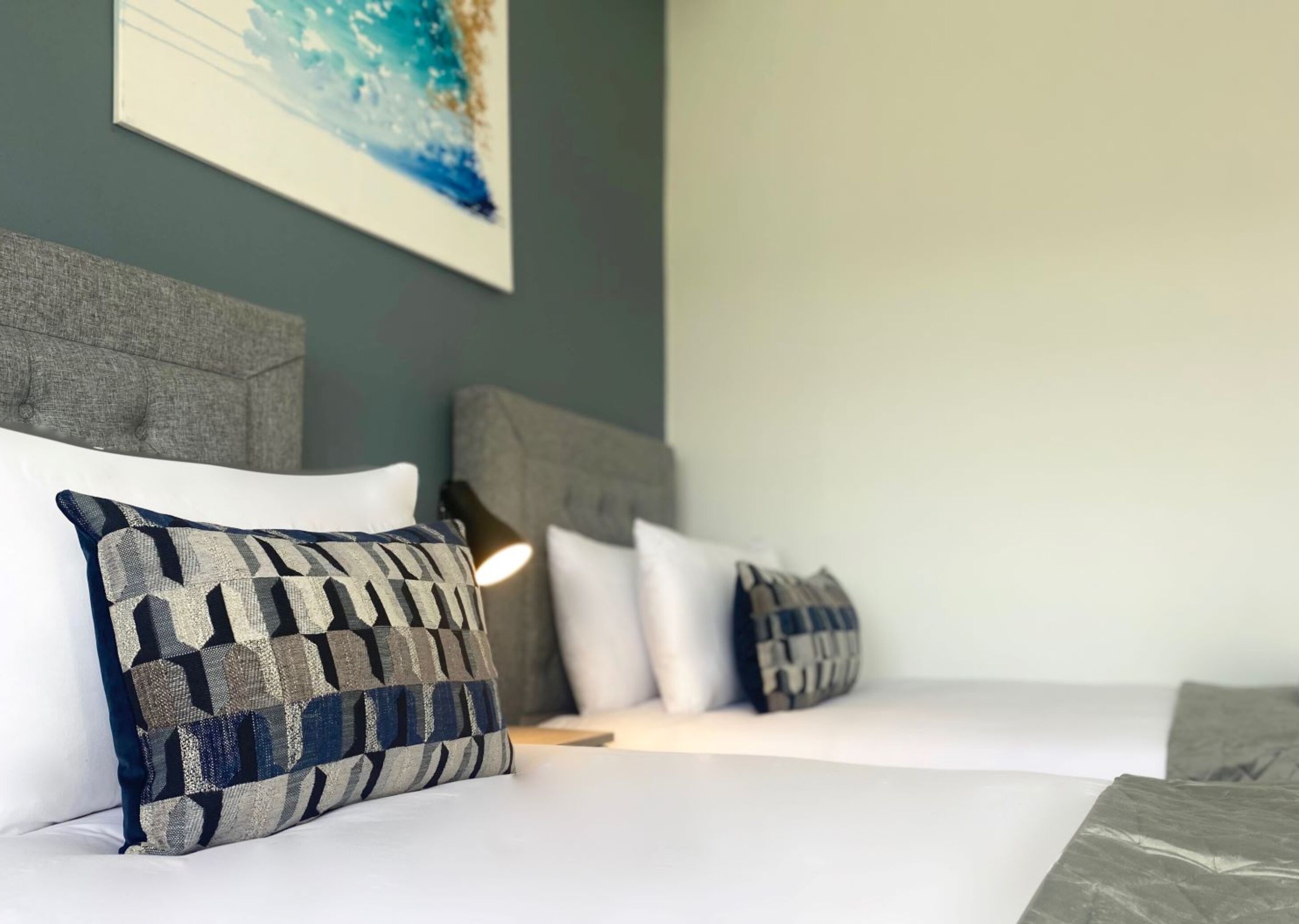 A neatly made bed with patterned pillows and a headboard against a wall with a framed artwork.