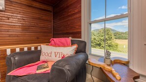 A cozy room with a leather chair, a window with a scenic view, and a wooden table with a guitar. - Charming Gingerbread House. Awesome mountain views near to SNP and Skyline Dr. (Penn Laird)