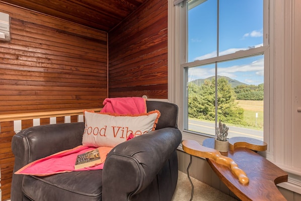 A cozy room with a leather chair, a window with a scenic view, and a wooden table with a guitar.