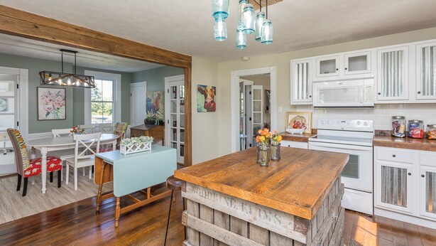 A kitchen with white cabinets, a wooden island, and a dining area with a blue table and chairs. - Charming Gingerbread House. Awesome mountain views near to SNP and Skyline Dr. (Penn Laird)