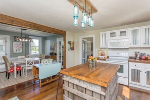Une cuisine avec des meubles blancs, un îlot central en bois et un coin repas comprenant une table et des chaises bleues.