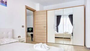Ein Hotelzimmer mit einem großen Bett, einem Nachttisch, einem Fernseher und einem Schrank mit Spiegel.