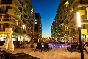 A nighttime view of a hotel with multiple high-rise buildings, a swimming pool, and outdoor seating areas with umbrellas. - Apartamente Indigo Alezzi (Navodari)