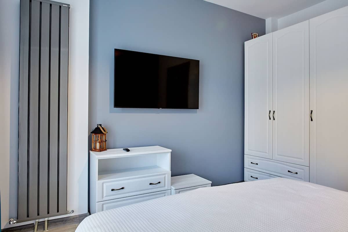 A bedroom with a bed, a TV mounted on the wall, a wardrobe, and a radiator.