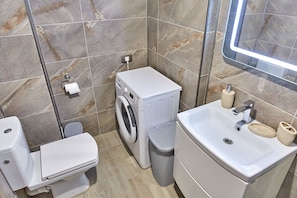 A bathroom with a toilet, washing machine, sink, and a mirror. - Apartamente Indigo Alezzi (Navodari)