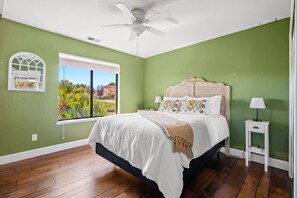 Ein Schlafzimmer mit einem Bett, einem Nachttisch, einem Fenster und einem Deckenventilator.