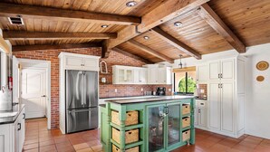Una cocina con pared de ladrillo, gabinetes blancos, una isla verde y un refrigerador de acero inoxidable.