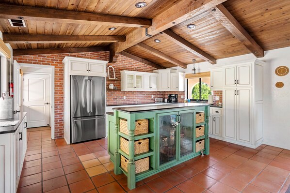 Una cocina con pared de ladrillo, gabinetes blancos, una isla verde y un refrigerador de acero inoxidable.