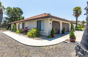 Ein einstöckiges Haus mit Ziegeldach, einer Garage und einem begrünten Vorgarten mit verschiedenen Sträuchern und einer Palme.
