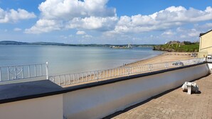 Um calçadão à beira-mar com calçada pavimentada, guarda-corpo branco e vista para o mar.