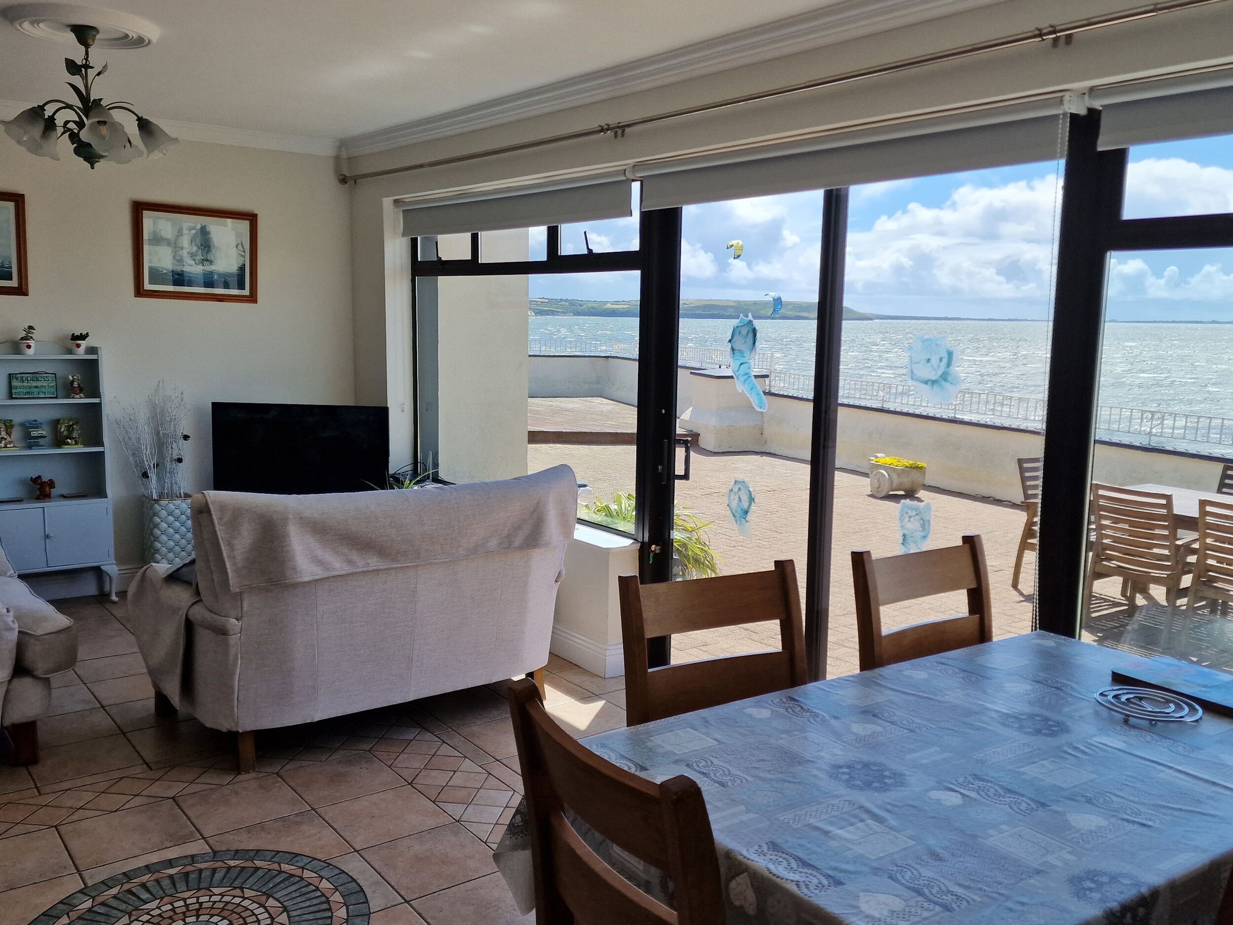 A dining area with a view of the sea, a sofa, a TV, and a bookshelf.