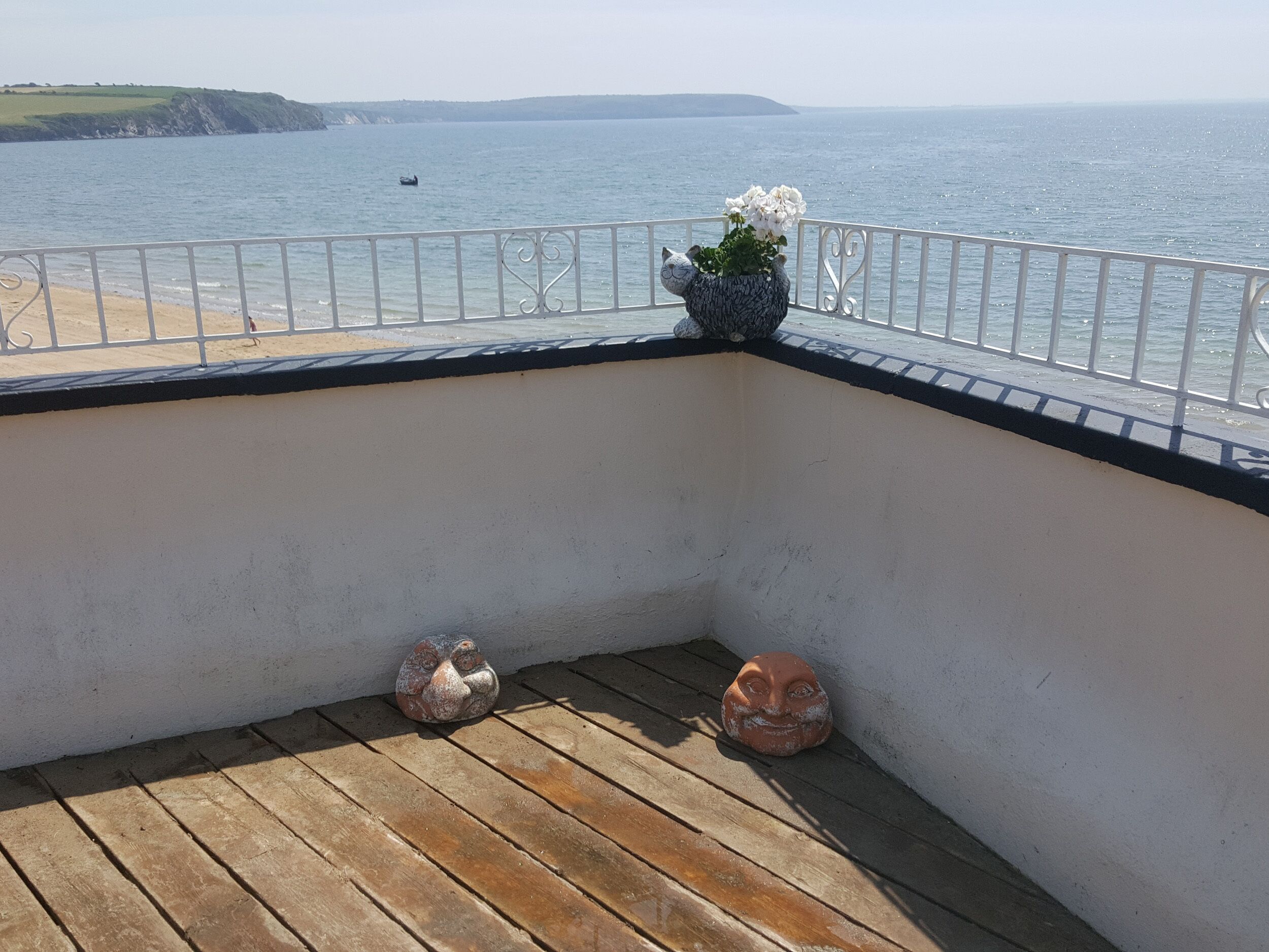 A balcony with a view of the sea, a white railing, and two decorative ceramic figures.