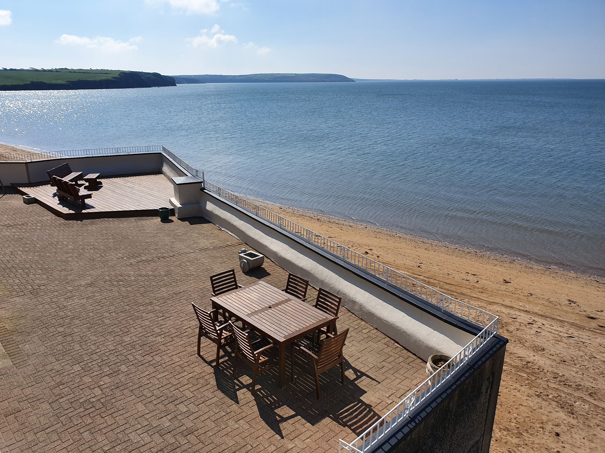Eine Terrasse im Freien mit Tisch und Stühlen, einer Betonbarriere und Blick auf das Meer.