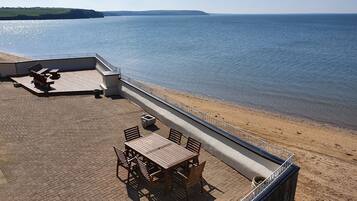 Eine Terrasse im Freien mit Tisch und Stühlen, einer Betonbarriere und Blick auf das Meer.
