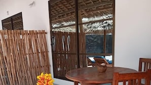 A wooden dining table with chairs, a potted plant, and a thatched roof structure. - Amani Paje B&B (Paje)