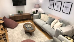 Un salon moderne avec un canapé gris, une table basse agrémentée d’objets décoratifs, un téléviseur fixé au mur et des œuvres d’art encadrées.