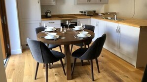Une cuisine moderne avec une table à manger ronde, dressée pour quatre personnes, et agrémentée d’assiettes, de bols et de verres à vin blancs.