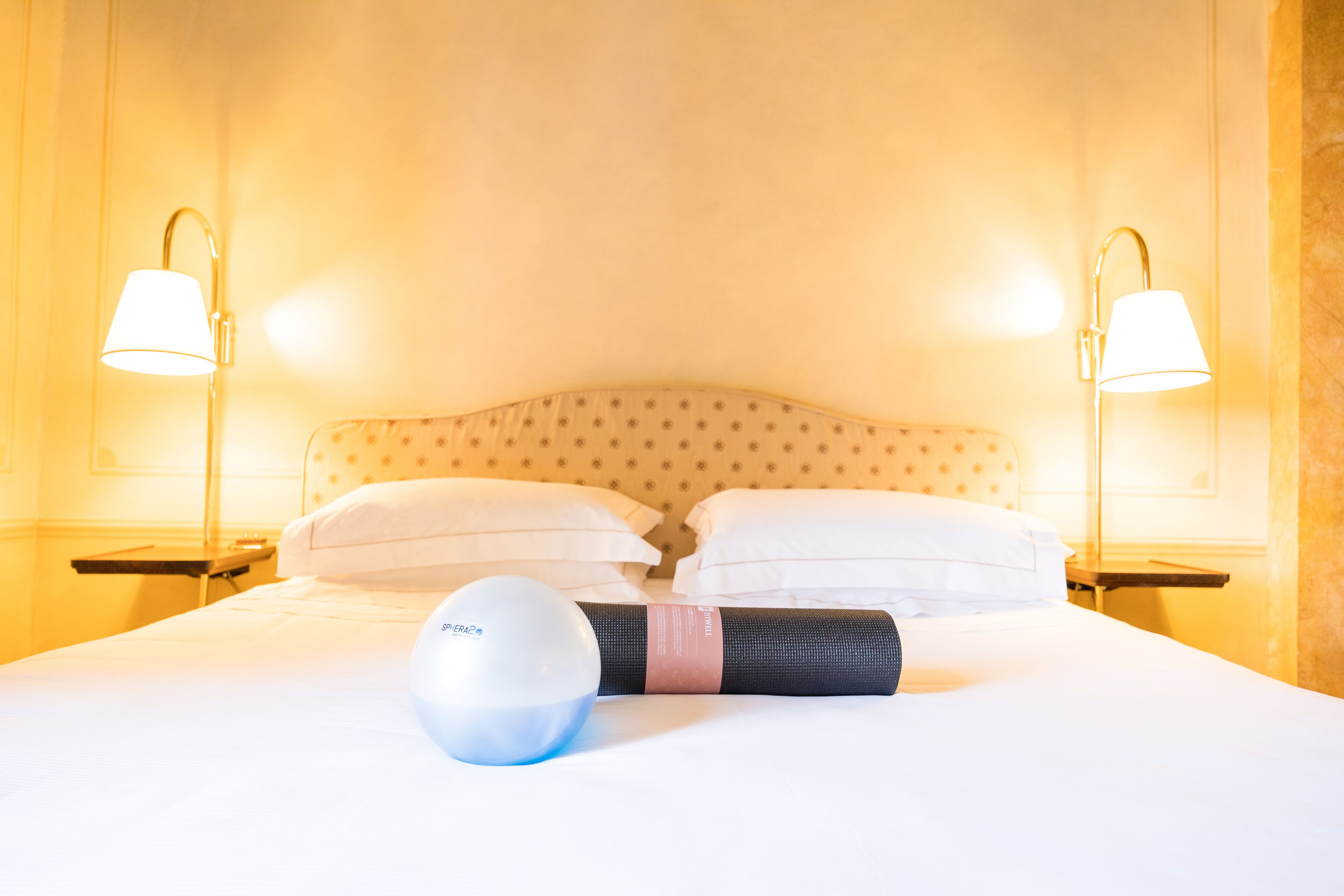 Une chambre d’hôtel avec un lit bien fait, deux lampes de chevet et un tapis de yoga.