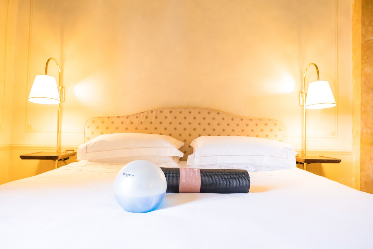 A hotel room with a neatly made bed, two bedside lamps, and a yoga mat.
