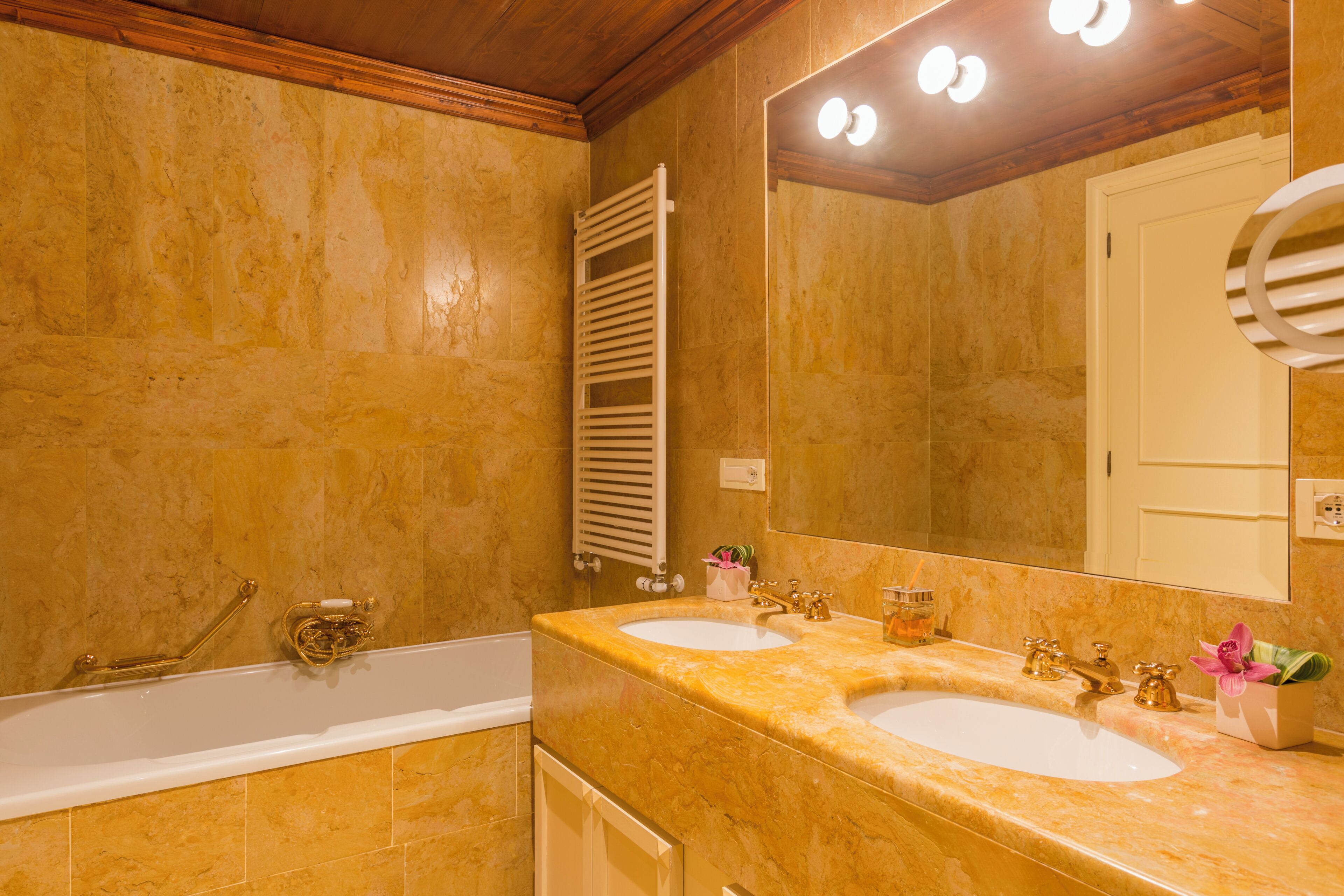 Une salle de bain avec deux lavabos, une baignoire, un porte-serviettes et un miroir avec éclairage intégré.