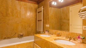 Une salle de bain avec deux lavabos, une baignoire, un porte-serviettes et un miroir avec éclairage intégré.